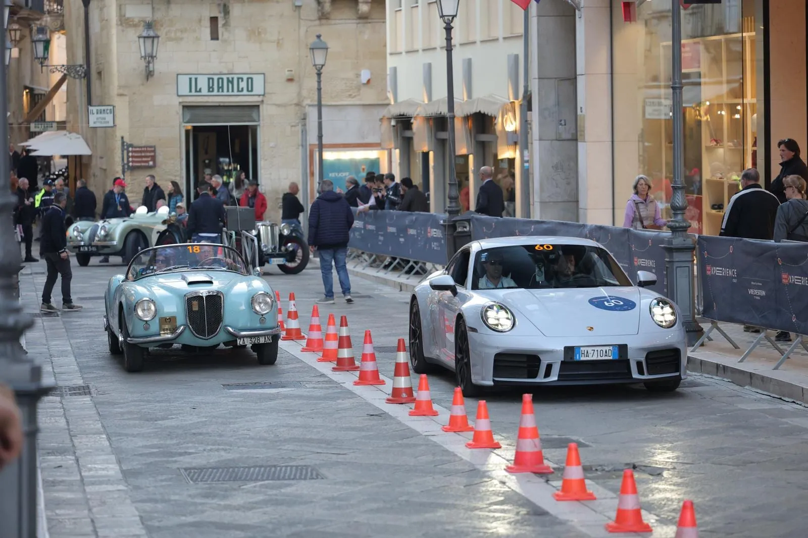 Car 60, a silver 2025 Porsche 911, in a timed trial between cones in a street in Lecce, with spectators behind the barriers